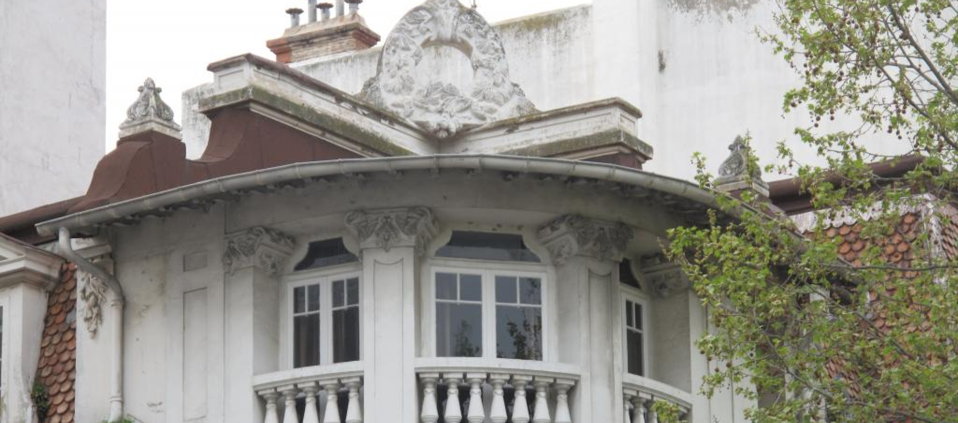  Angle du dernier niveau traité en courbe : 3 fenetres , balcons a balustres, sur le toit une couronne de branches de pin 